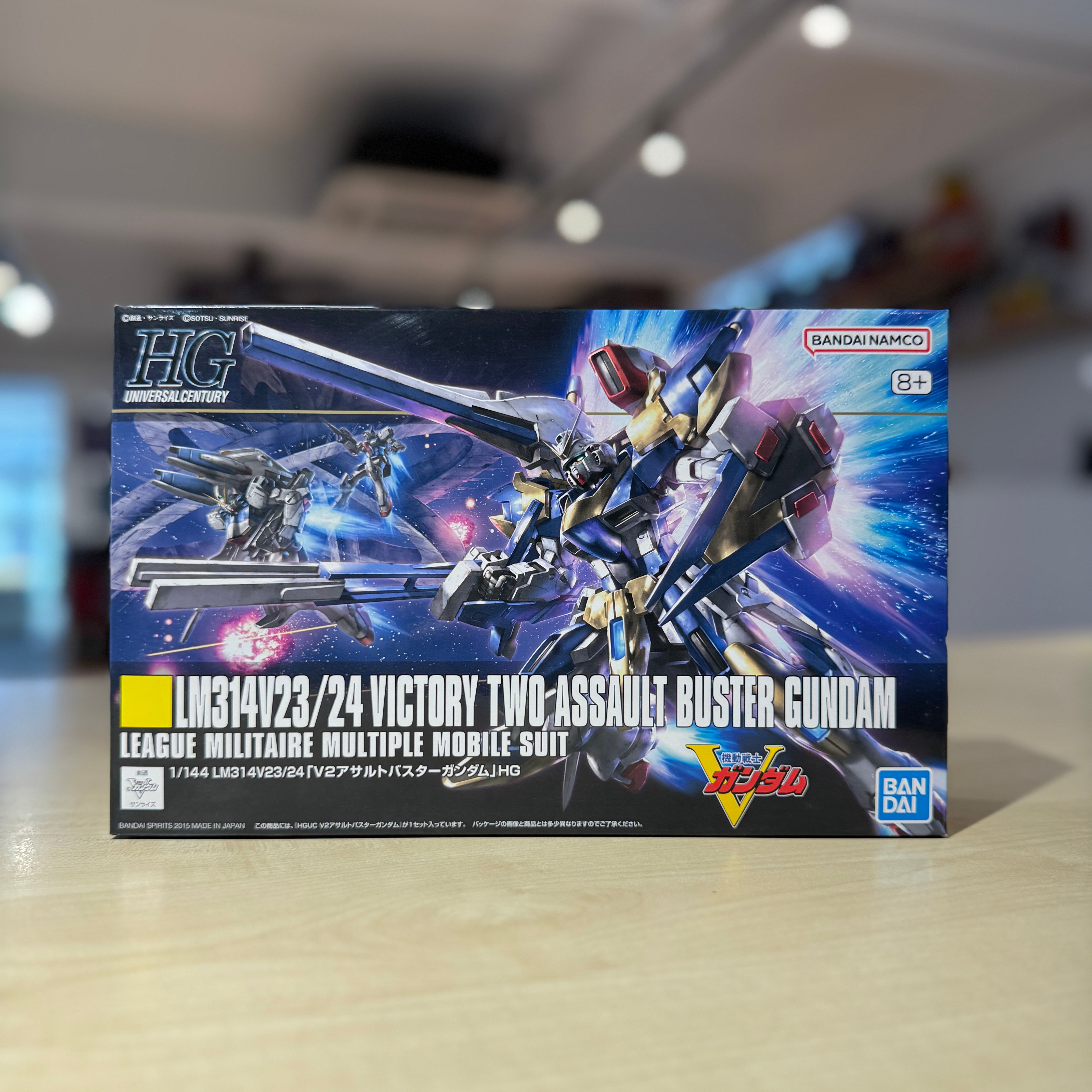 Model kit packaging of a HGUC V2 Assault Buster Gundam on a blurred indoor background