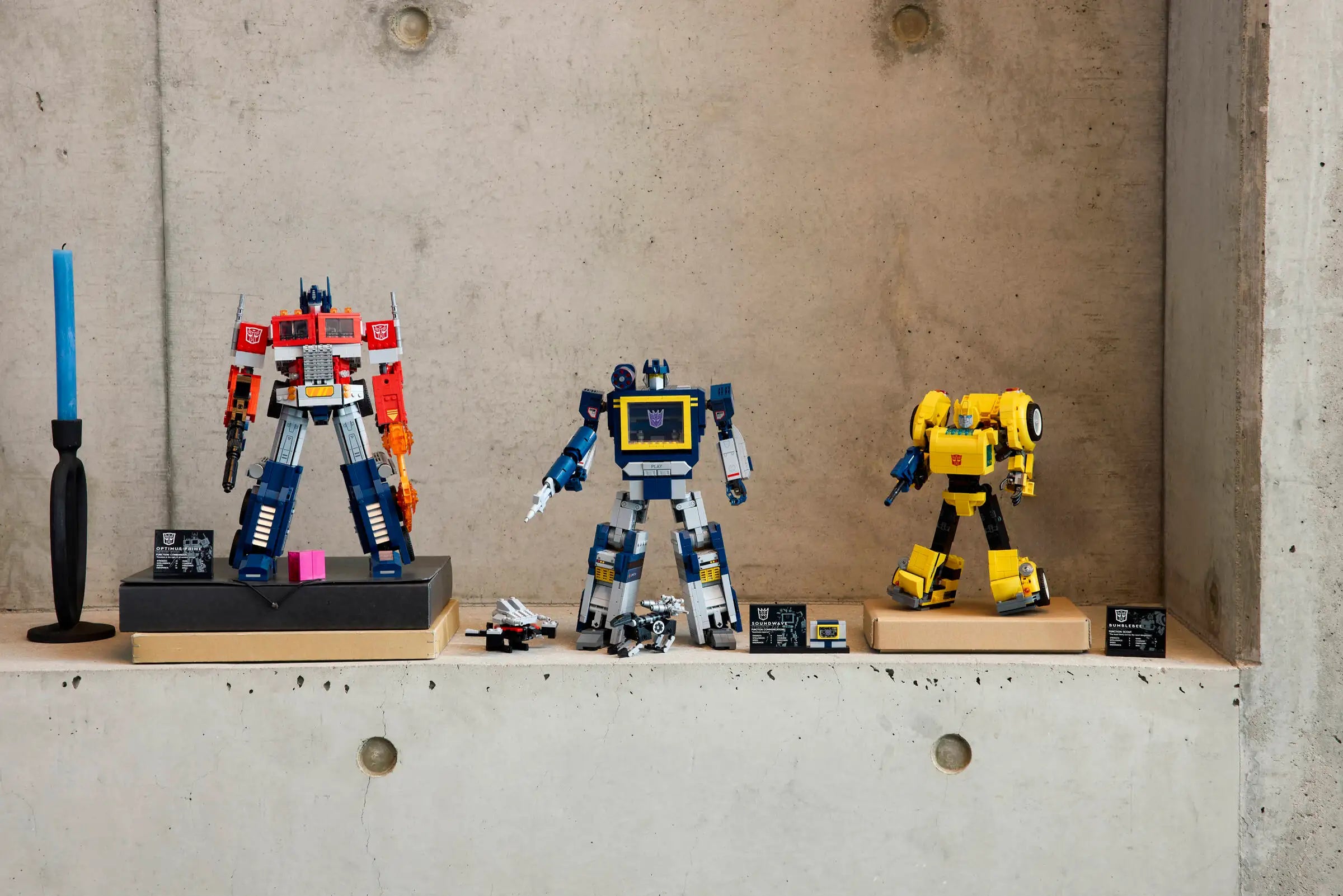 Three LEGO Transformer sets on a concrete surface with a candle in the background.