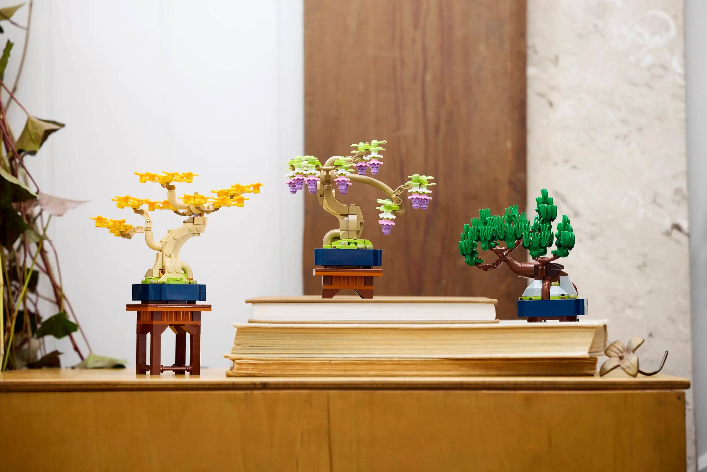 Three LEGO bonsai tree sets on a wooden surface with a neutral background