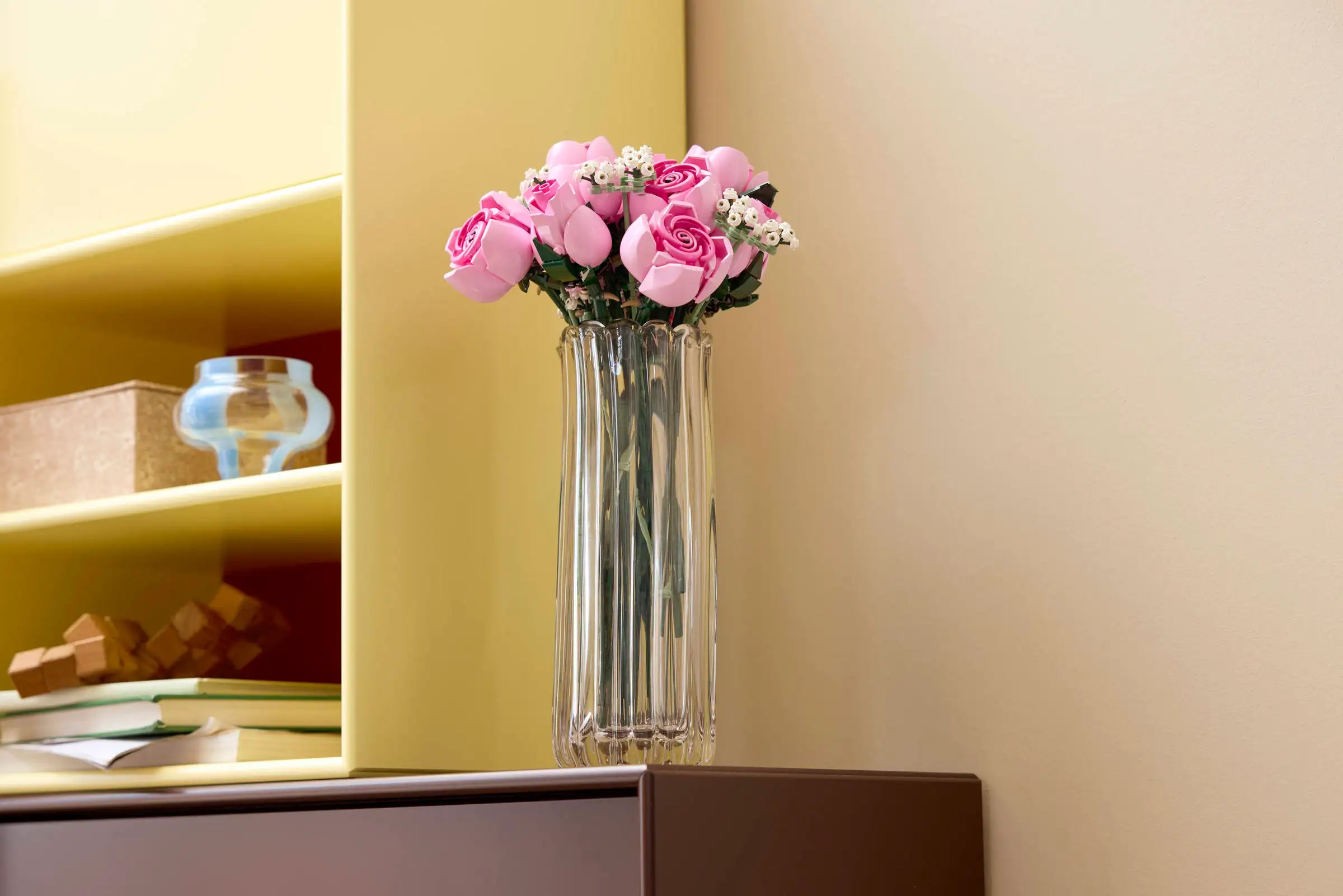Clear vase with LEGO 10374 Bouquet of Pink Roses flowers on a shelf against a beige wall