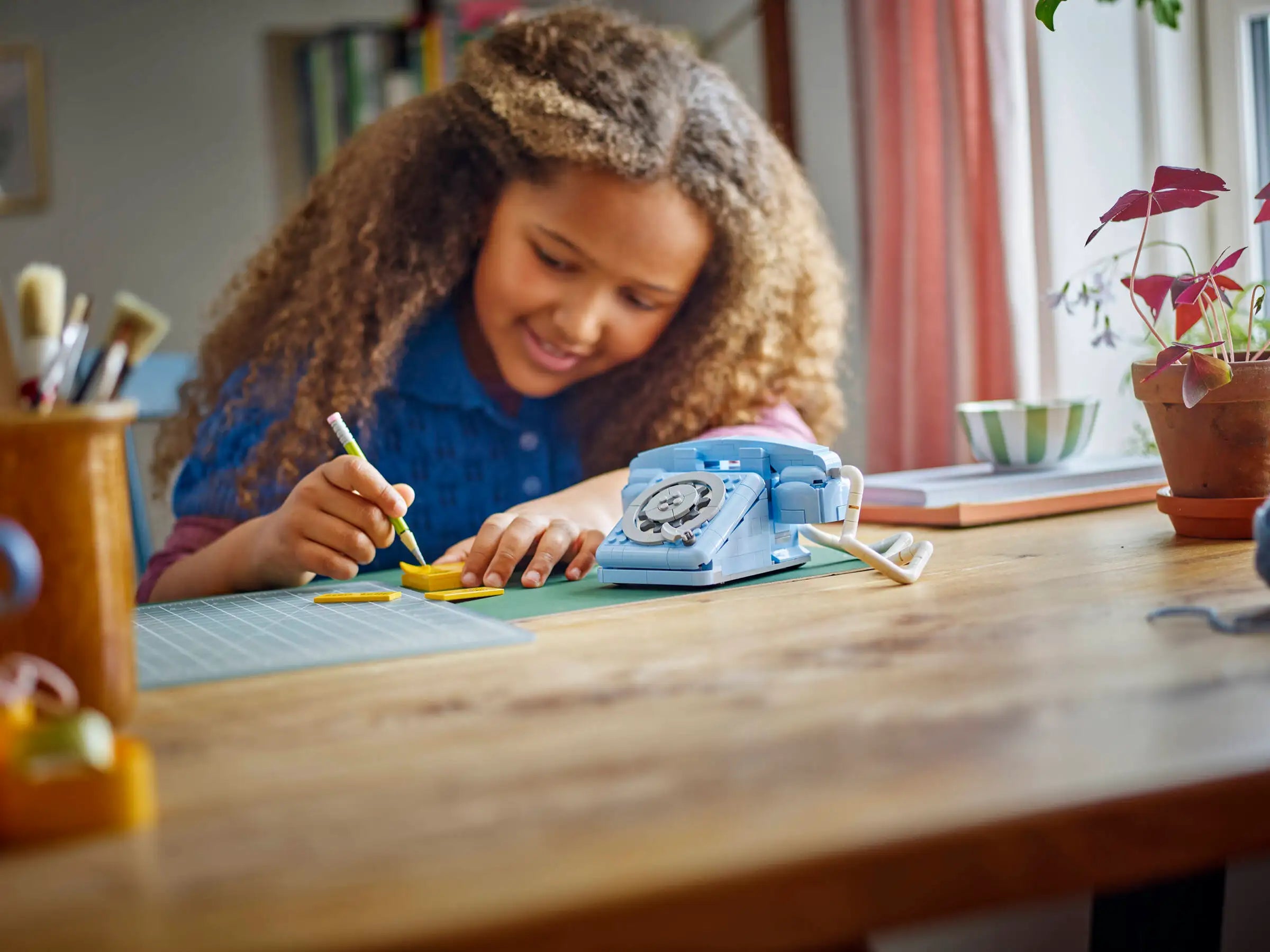 Child drawing at a desk with a toy phone and stationery - LEGO 31174 Retro Telephone