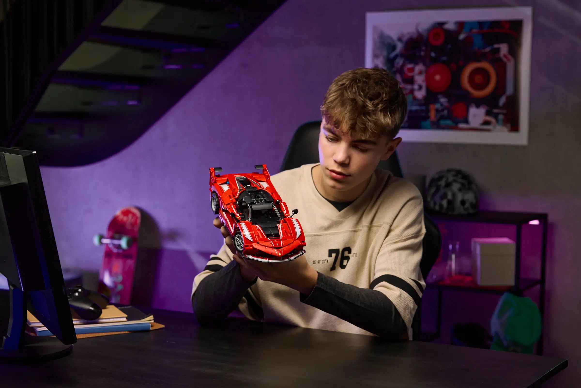 Young boy holding a LEGO 42212 Ferrari FXX K red sport car in a room with purple walls and various items on shelves.