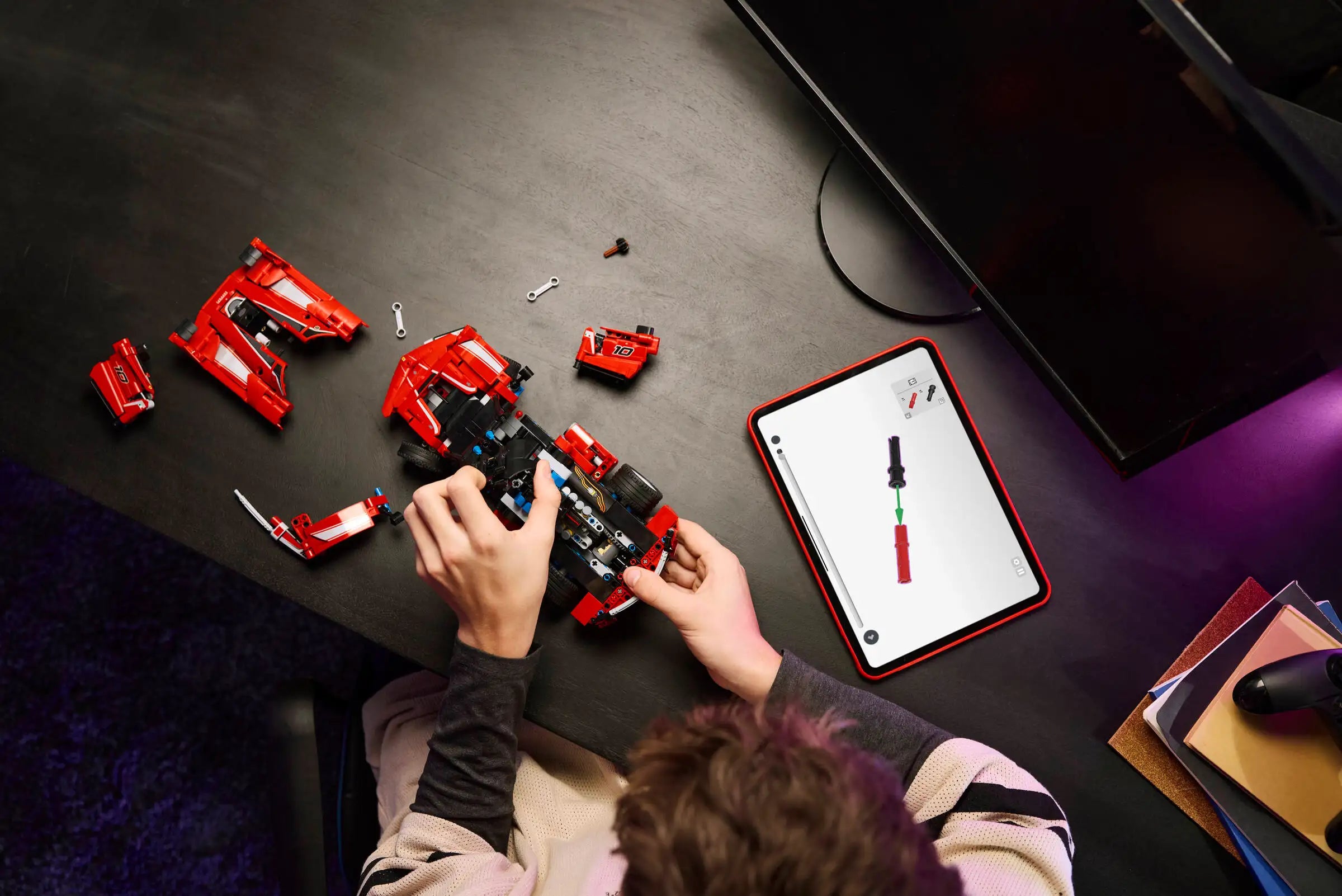 Person assembling a r LEGO 42212 Ferrari FXX K set with a tablet showing instructions on a dark surface.