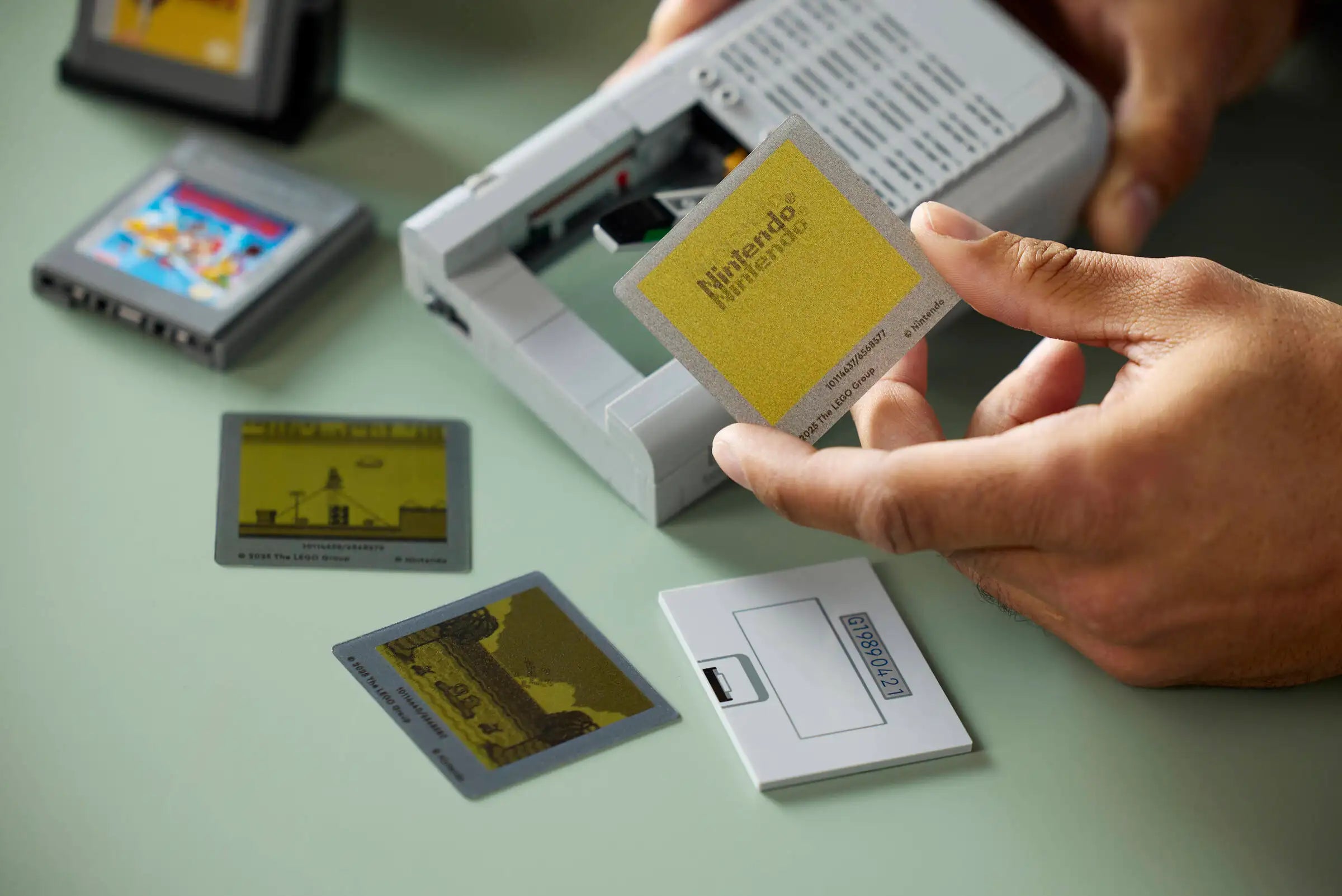 Person holding a LEGO 72046 Game Boy cartridge with other cartridges on a light green surface