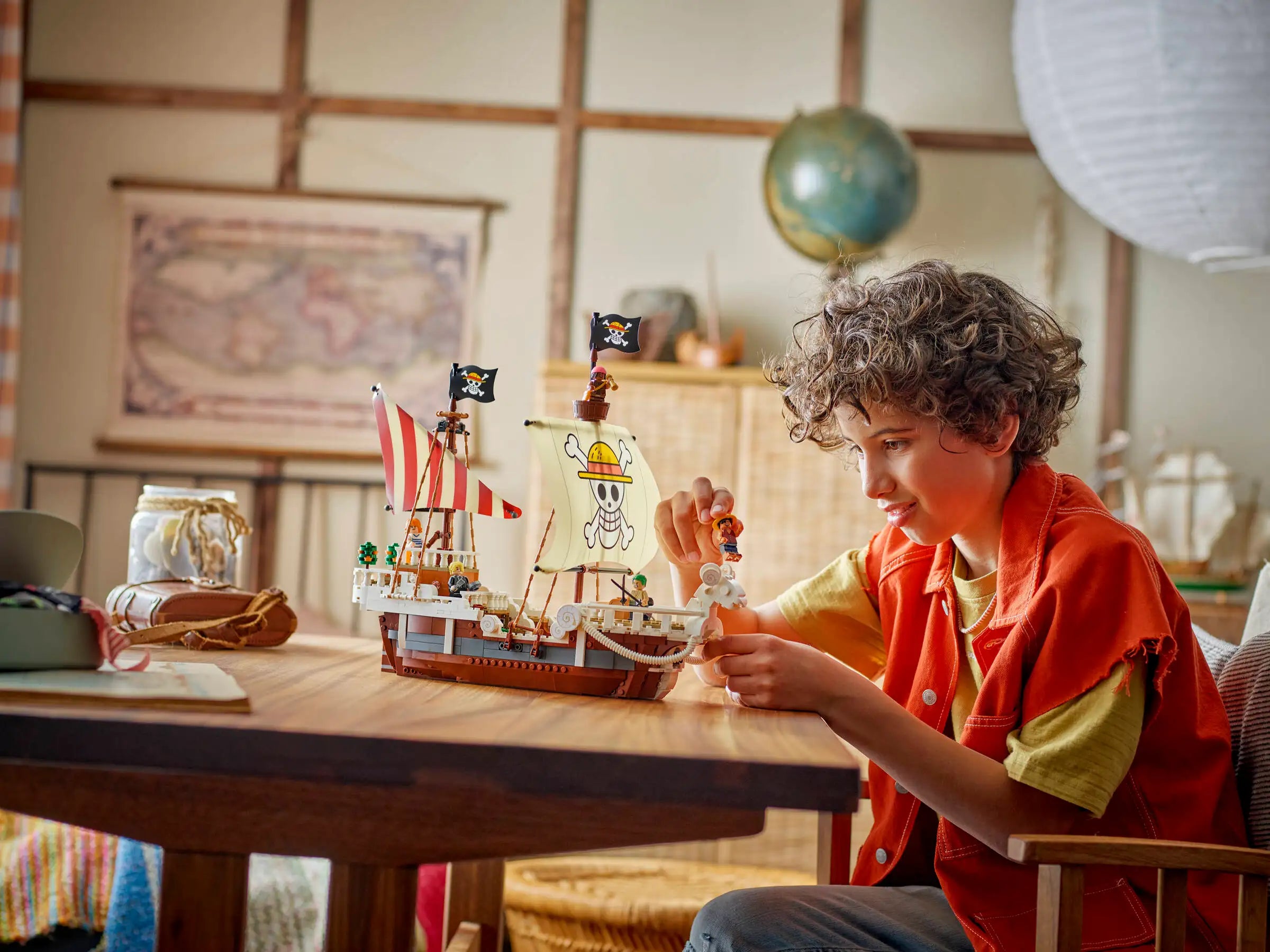 Child playing with LEGO 75639 The Going Merry Pirate Ship at a table in a room with a map and globe on the wall.