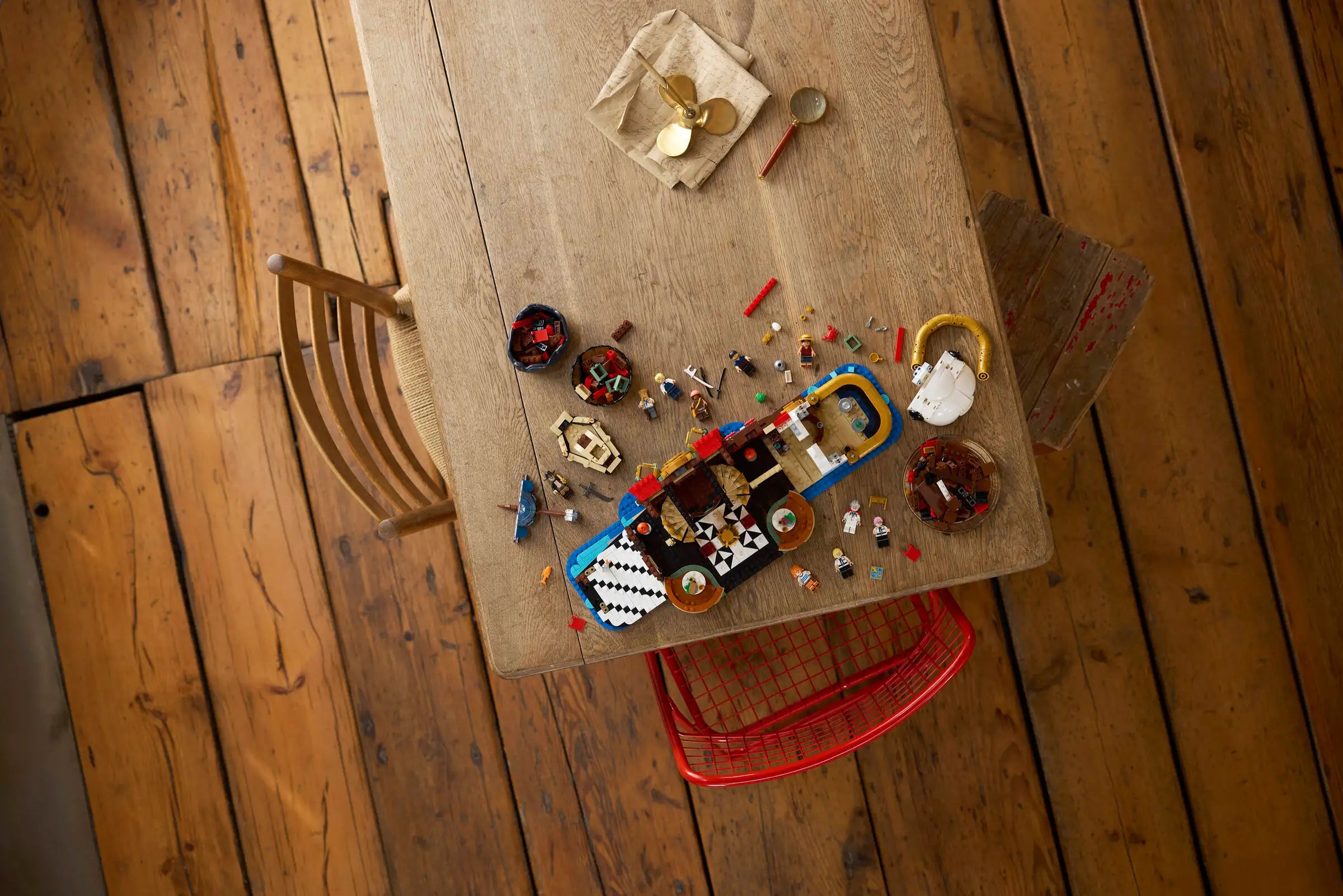 Top-down view of a LEGO 75640 The Baratie Floating Restaurant with various small items on it, including a red chair partially visible.