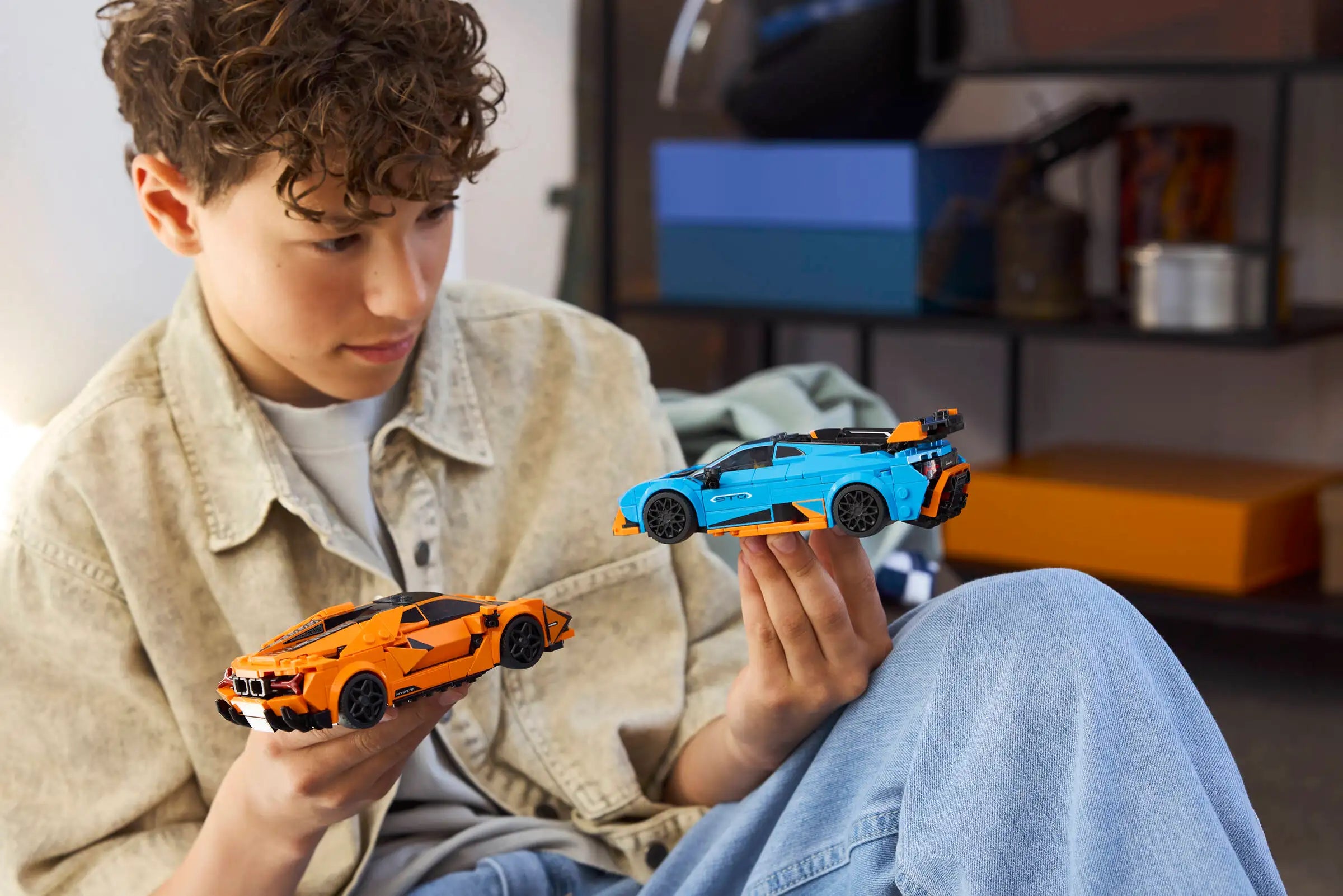 Child holding two toy cars in a room with shelves in the background - LEGO 77238 Lamborghini Revuelto & Lamborghini Huracán STO
