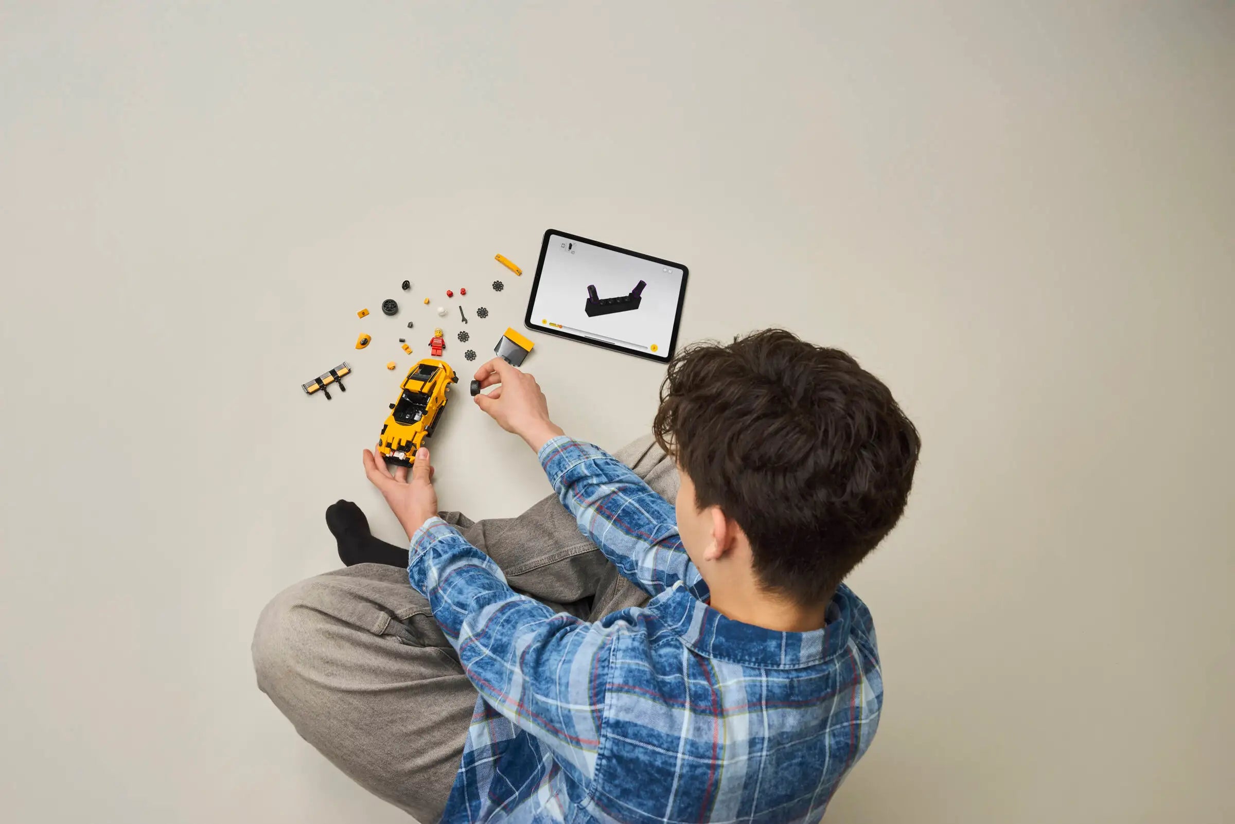 Person sitting on the floor with LEGO 77239 Porsche 911 GT3 RS and a tablet displaying assembly manual.