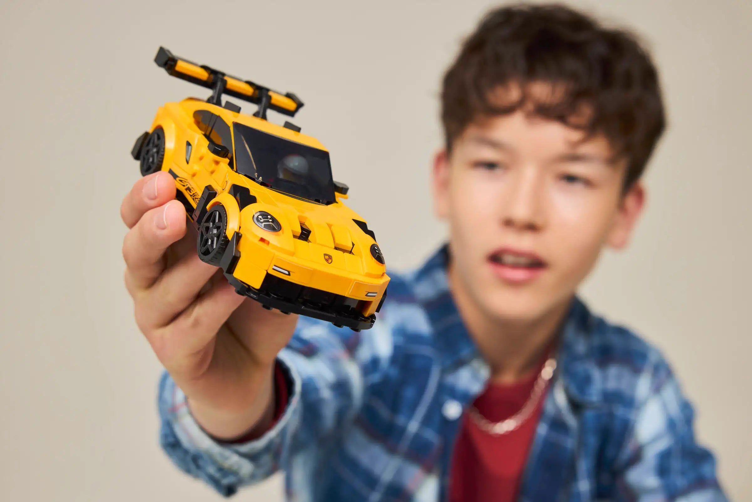 Child holding a LEGO 77239 Porsche 911 GT3 RS against a plain background
