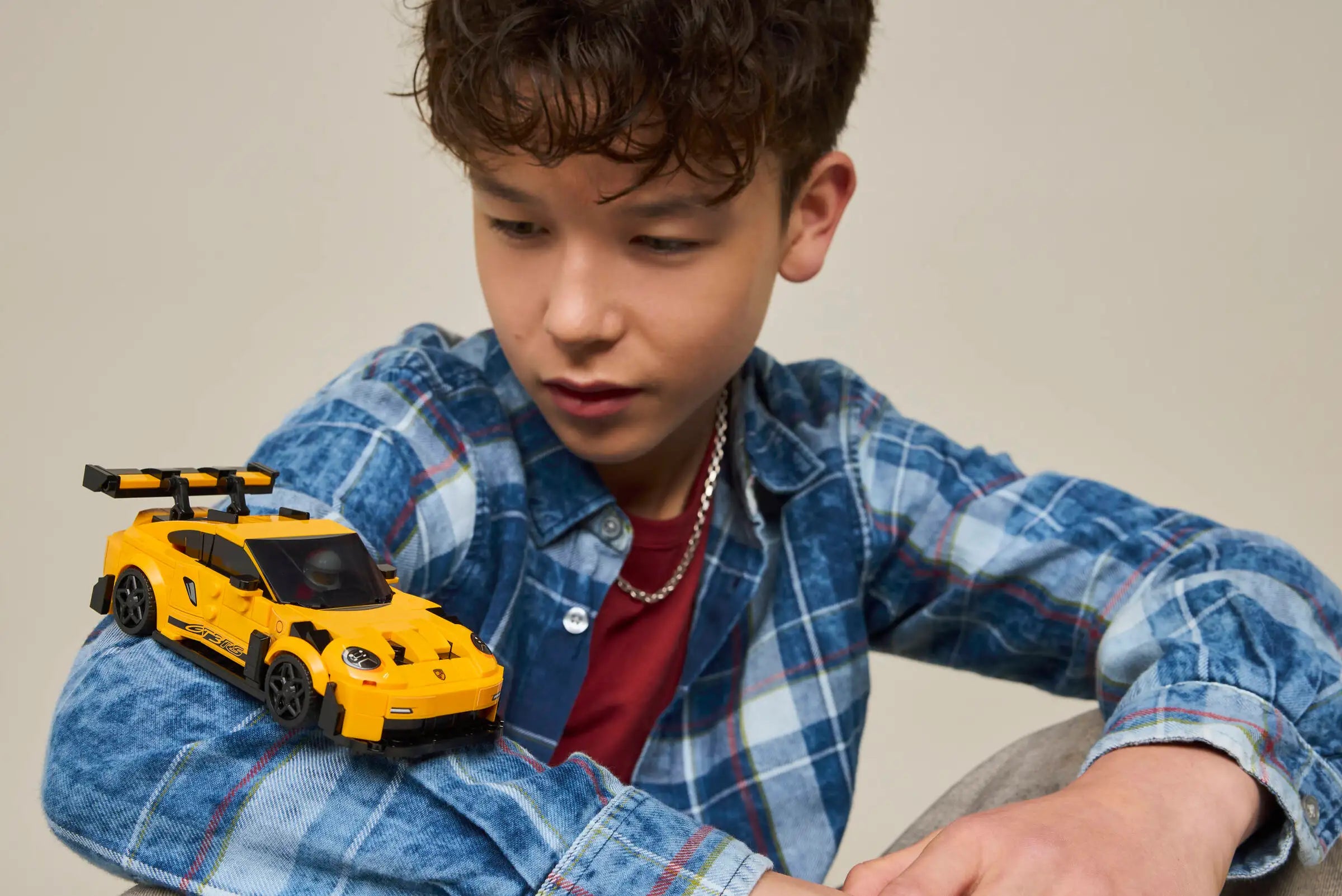 Child holding a LEGO 77239 Porsche 911 GT3 RS yellow toy car against a neutral background