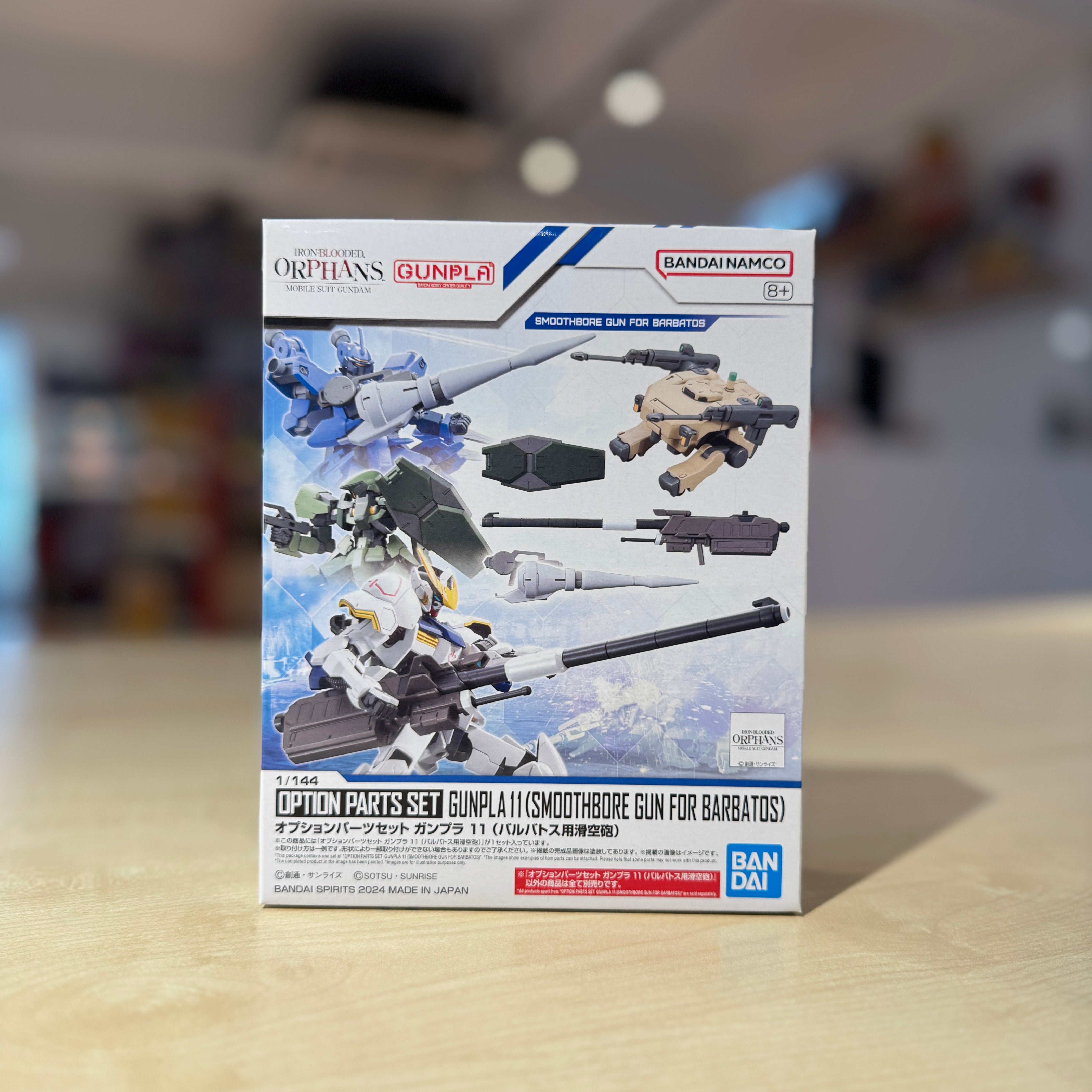 Model kit packaging for Option Parts Set Gunpla 11 (Smoothbore Gun for Barbatos) with Orphans Gunpla branding on a blurred background