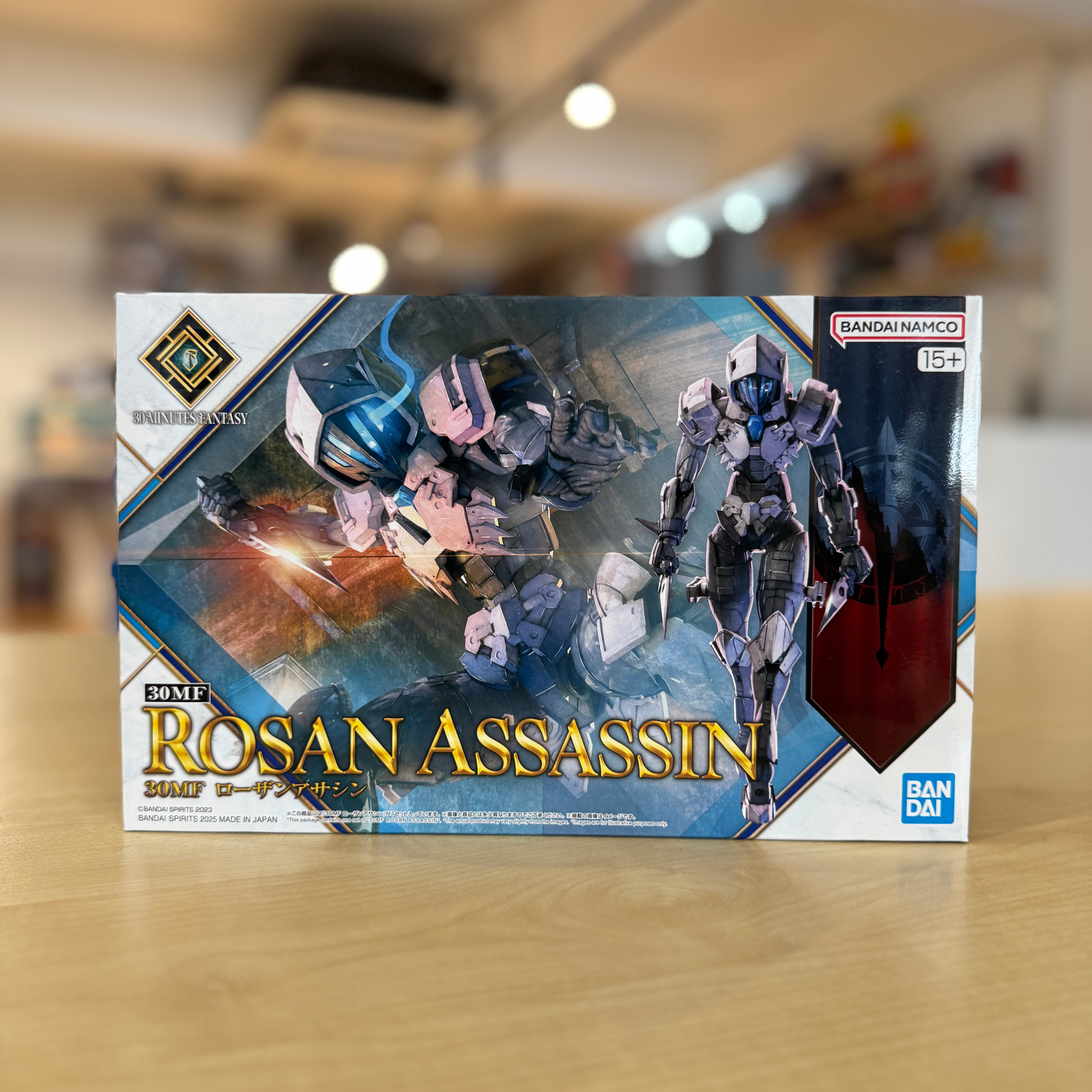 Box of Rosan Assassin model kit by Bandai on a wooden surface with a blurred background