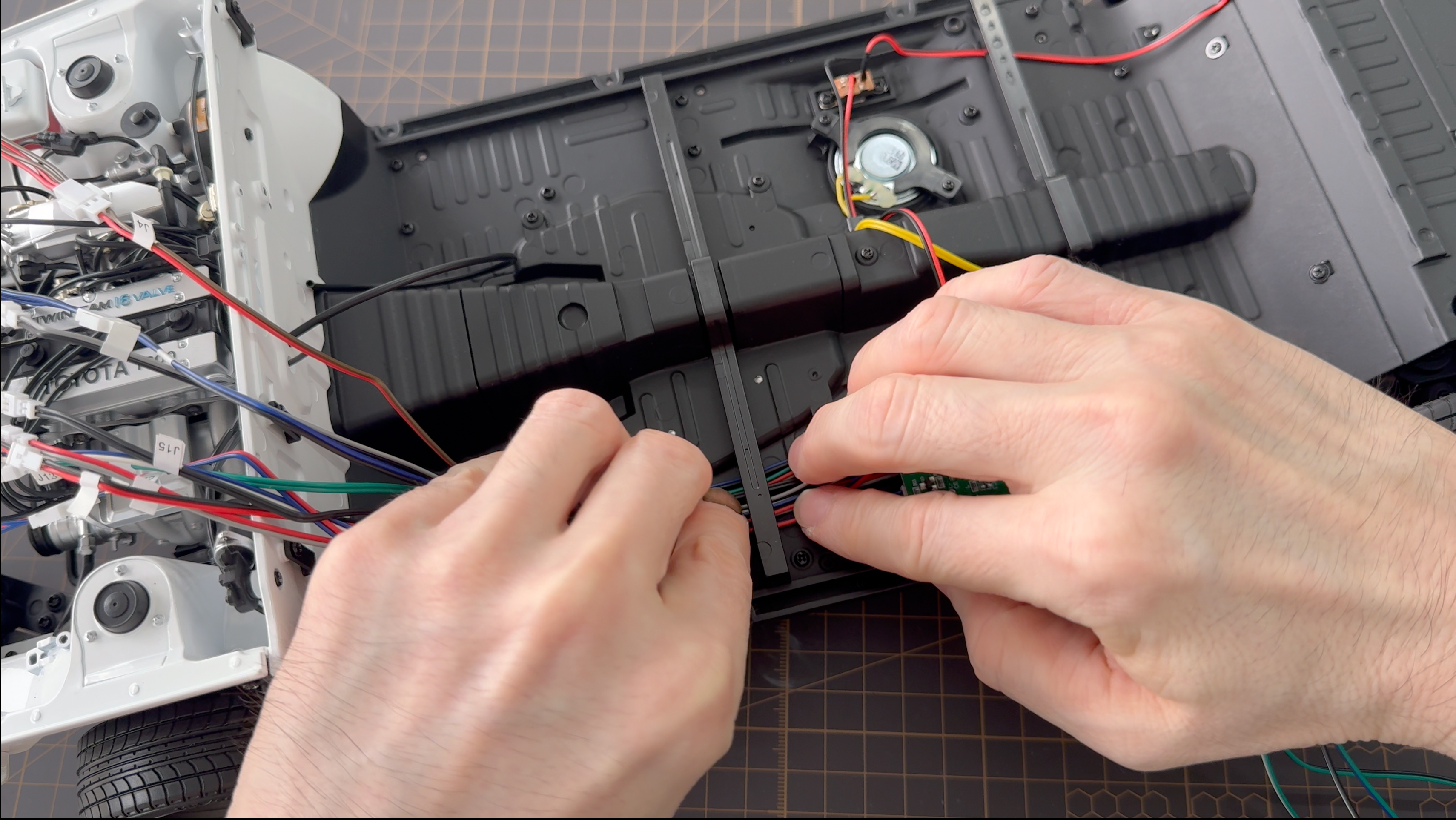 Close-up of a person's hands connecting multicolored wires to a black electronic control module inside a vehicle chassis.