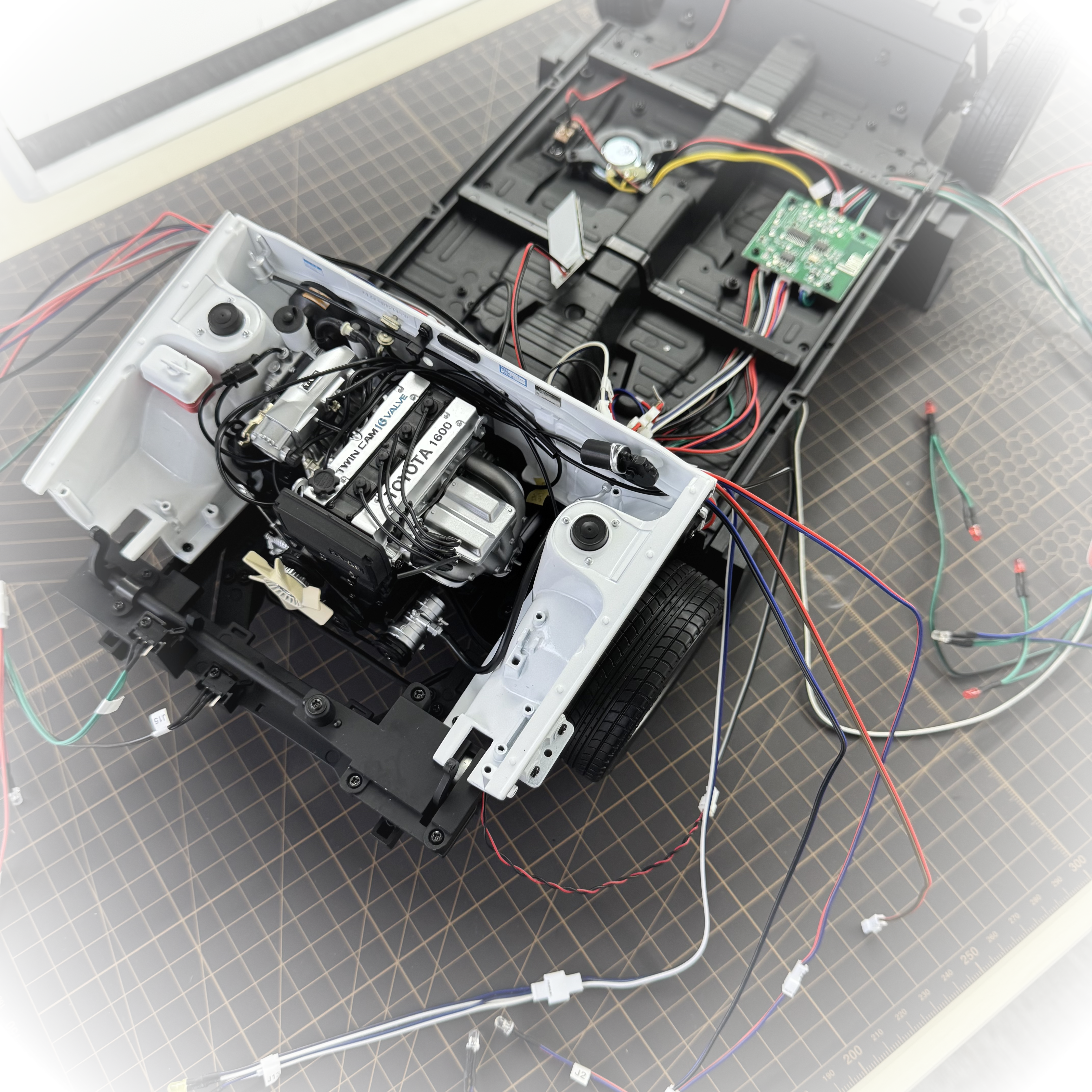 An open electric vehicle battery pack module showing internal wiring, electronic control boards, and battery cells, placed on a gridded cutting mat. - DeToyz Studio Transparent.