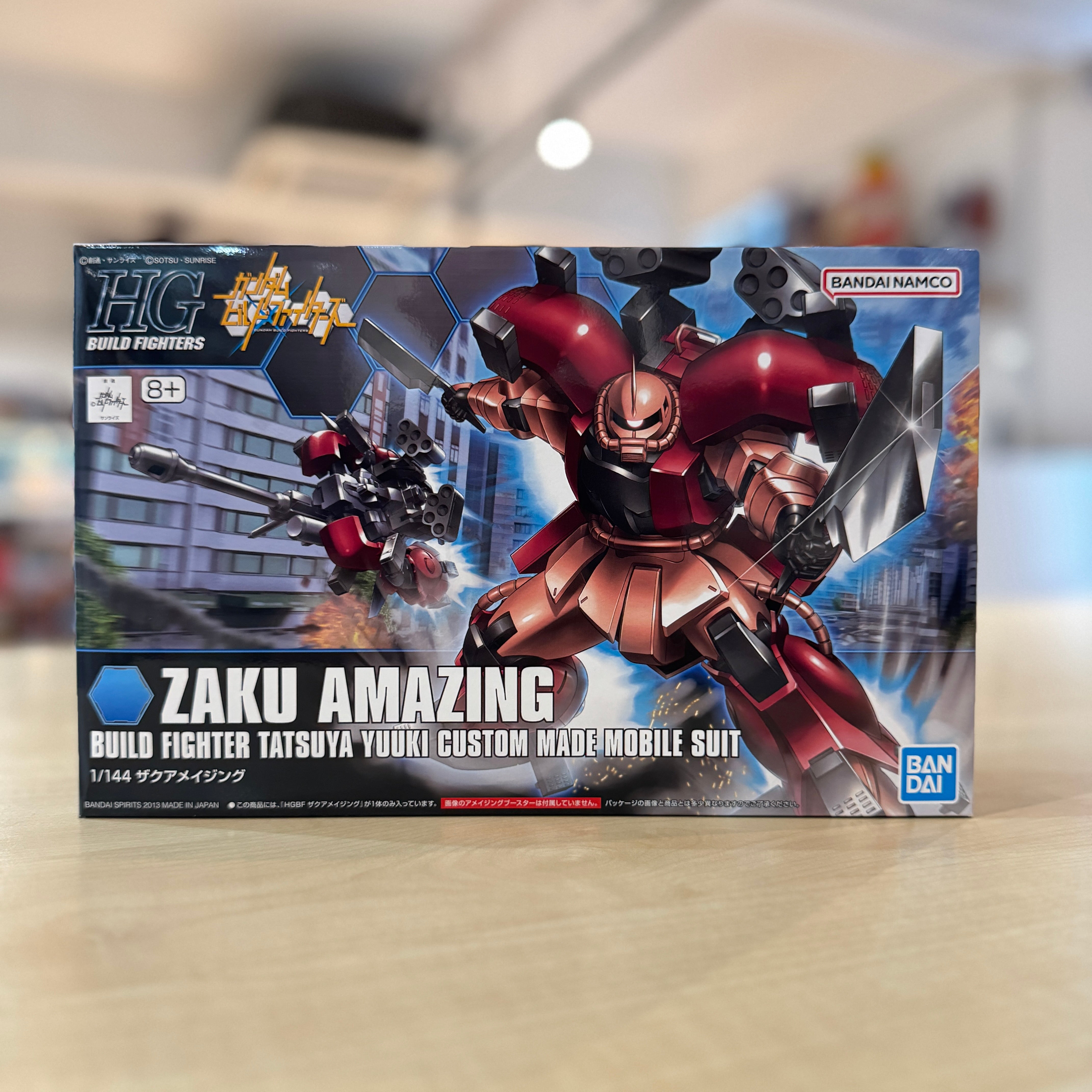 Boxed model kit of a robot with HGBF Zaku Amazing branding on a blurred indoor background