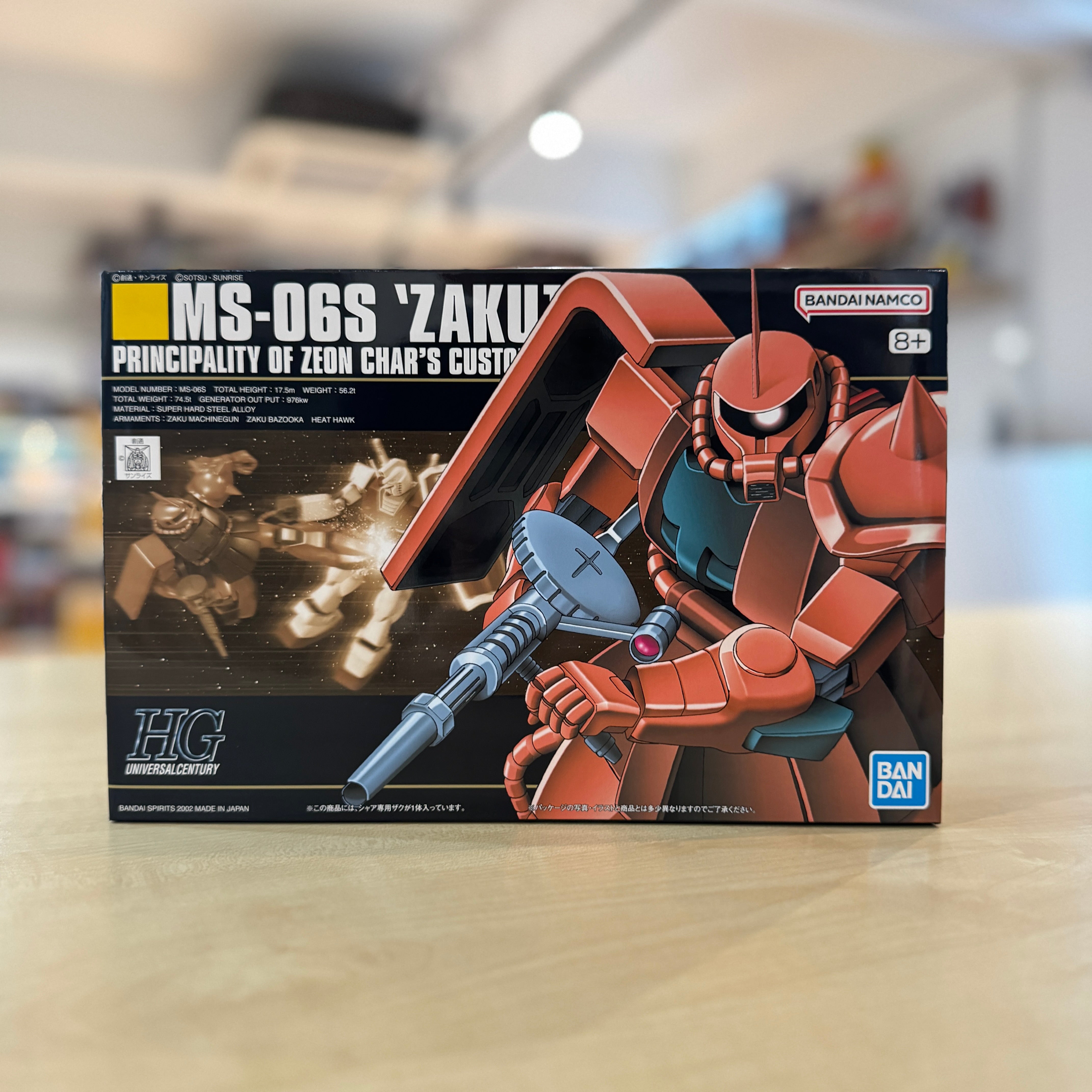 Model kit box for HGUC MS-06S Char's Zaku II Custom from Bandai on a blurred indoor background