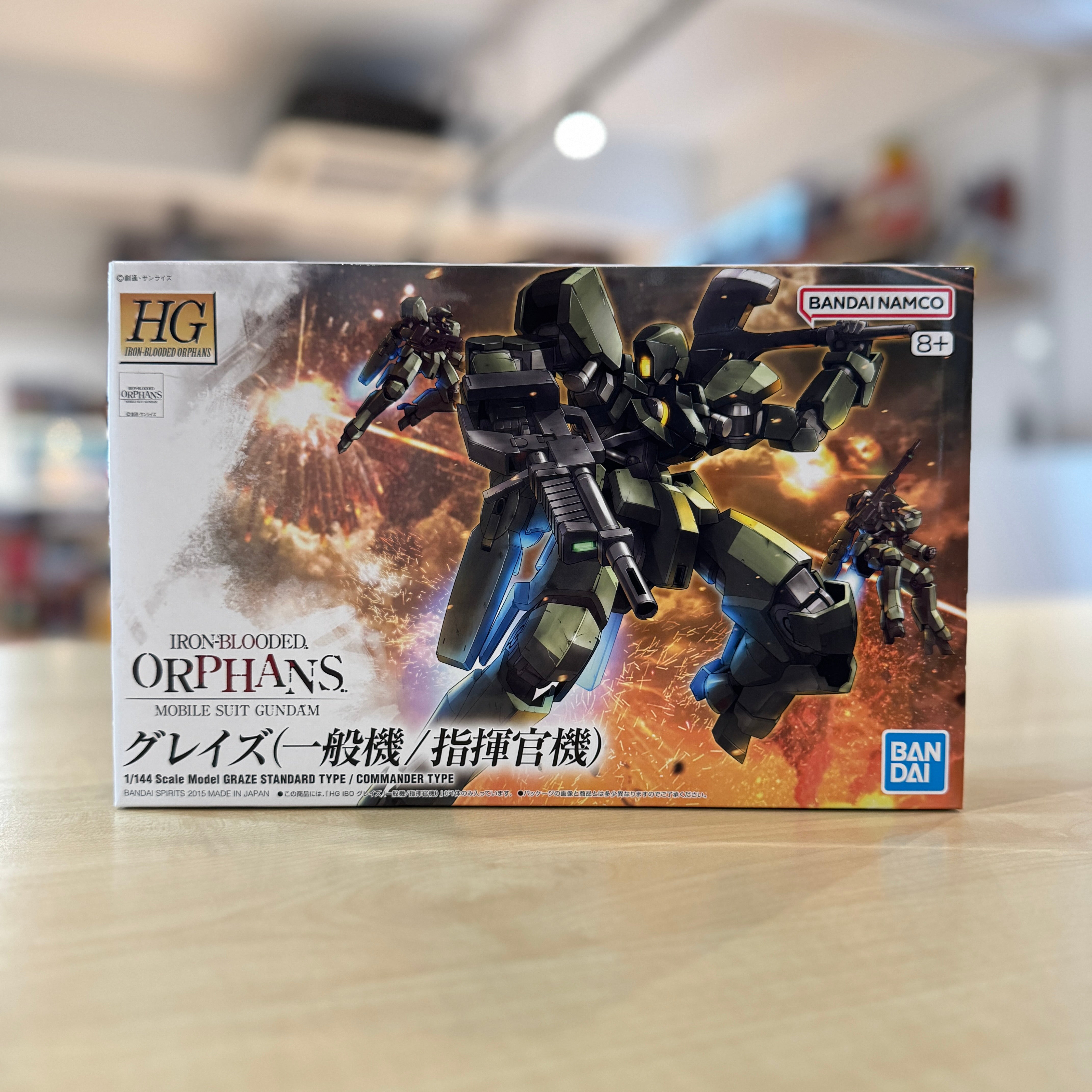 Model kit packaging for HG Graze (Standard Type/Commander Type) with robot illustration on a blurred indoor background