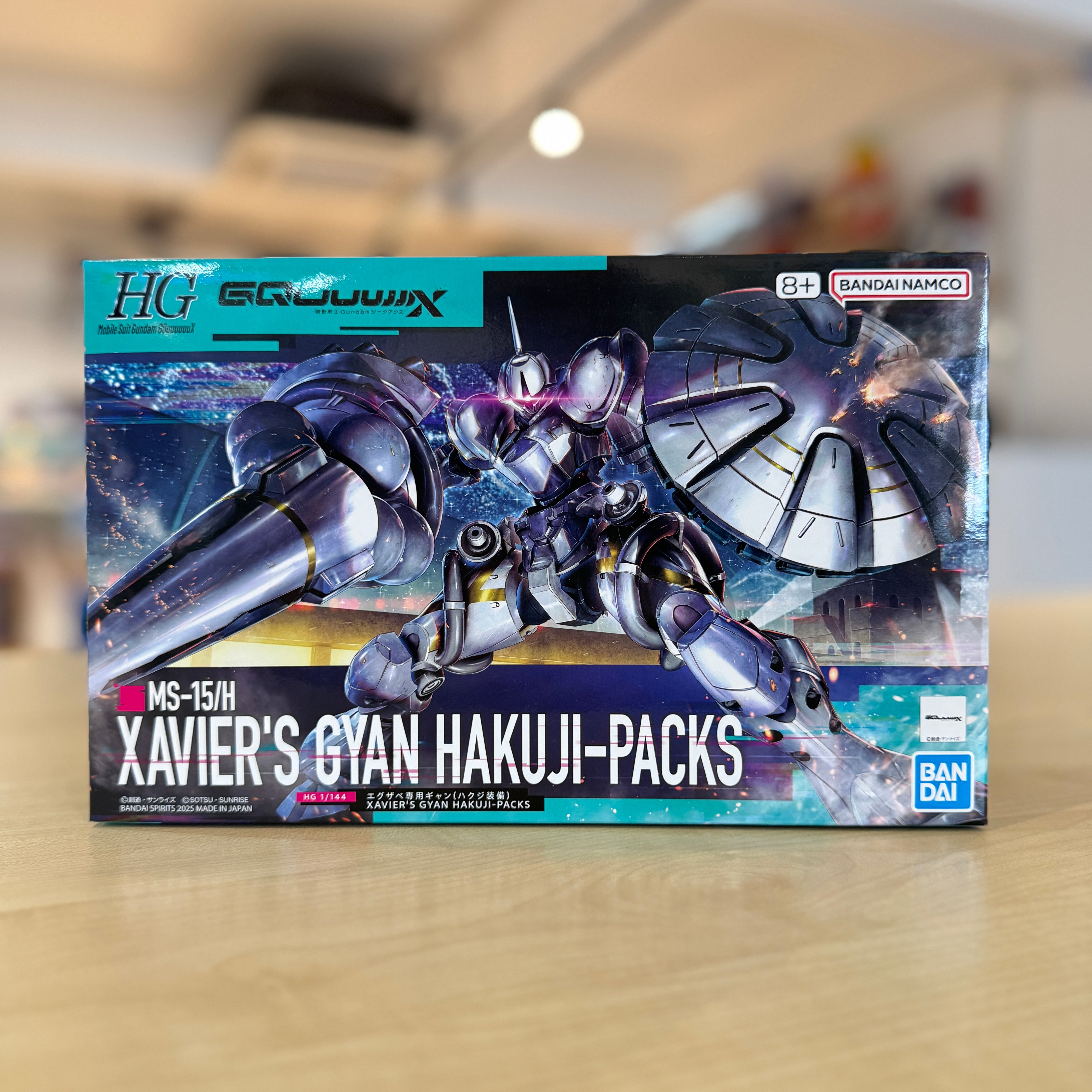 Model kit packaging for 'Xavier's Gyan Hakuji-Packs' with Bandai branding on a blurred indoor background.