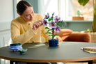 Woman arranging LEGO 10372 Hibiscus flowers in a pot on a table indoors