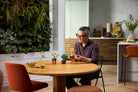 Man sitting at a wooden table in a modern kitchen with plants and decor, playing LEGO 10373 Mini Bonsai Trees set.