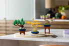Three LEGO models of bonsai trees on a marble surface with a blurred indoor background.