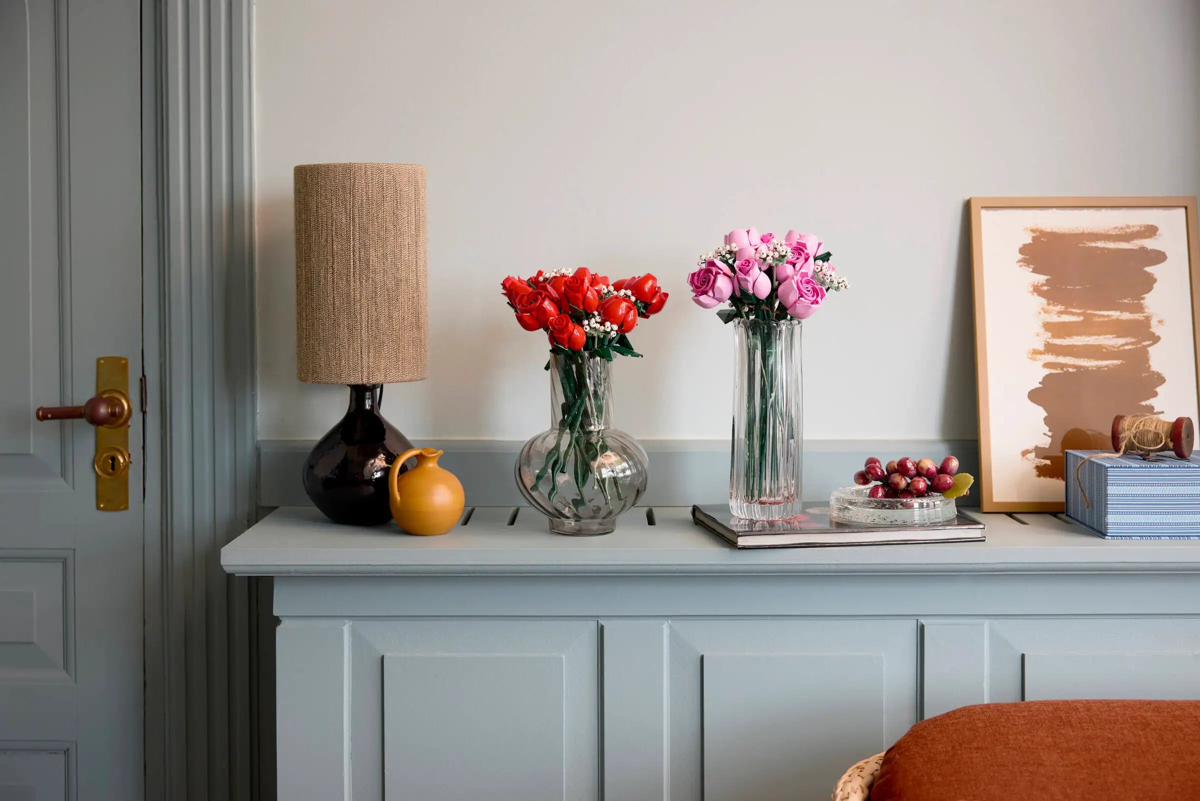 Decorative shelf with a lamp, LEGO 10374 Bouquet of Pink Roses, and books against a light gray wall.