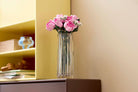 Clear vase with LEGO 10374 Bouquet of Pink Roses flowers on a shelf against a beige wall