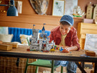 Child playing with a LEGO 31168 Medieval Horse Knight Castle set at a table in a cozy room.