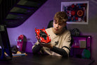 Young boy holding a LEGO 42212 Ferrari FXX K red sport car in a room with purple walls and various items on shelves.