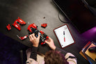 Person assembling a r LEGO 42212 Ferrari FXX K set with a tablet showing instructions on a dark surface.