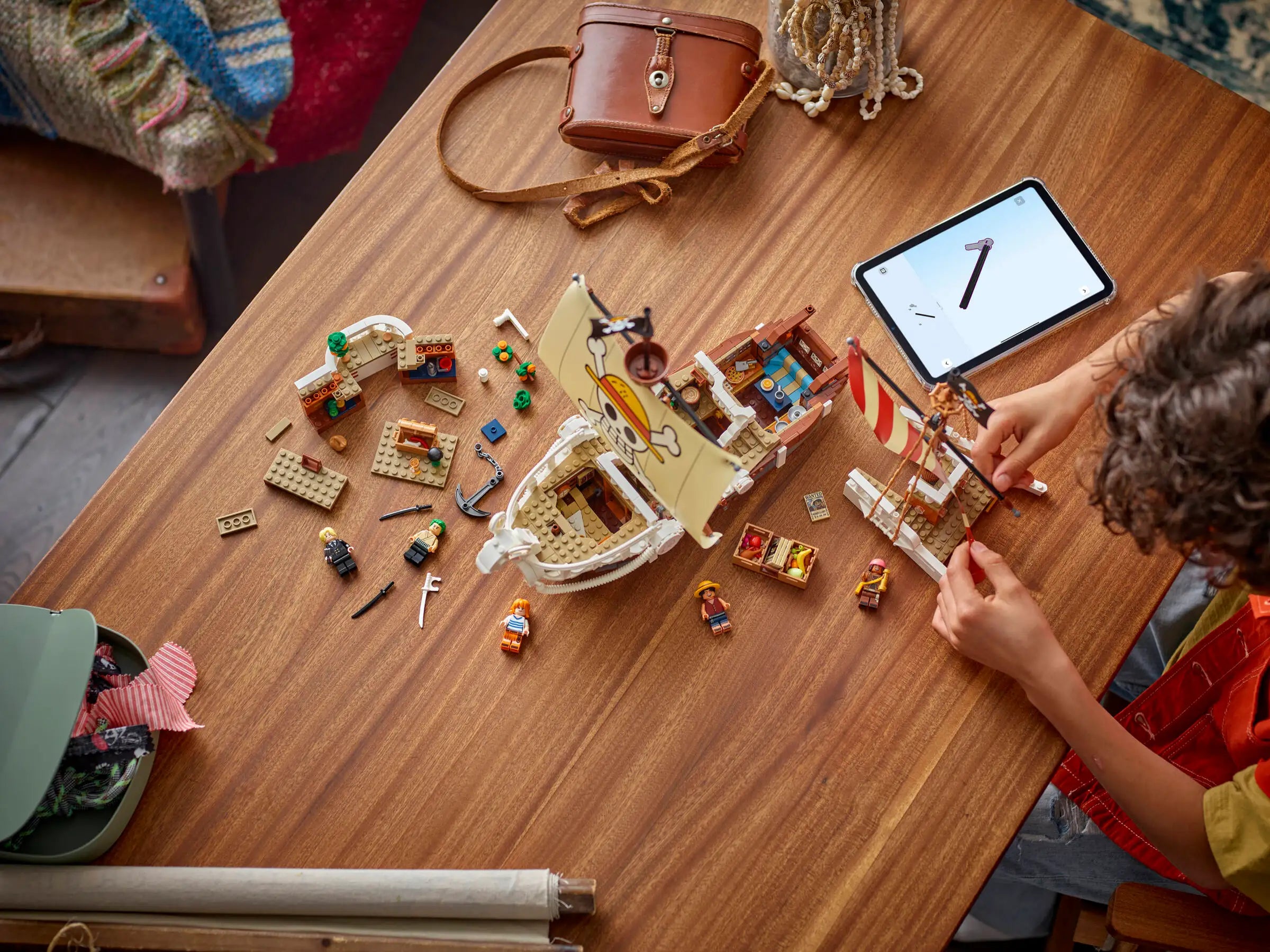 Child playing with LEGO 75639 The Going Merry Pirate Ship on a wooden table with a tablet displaying a clock.