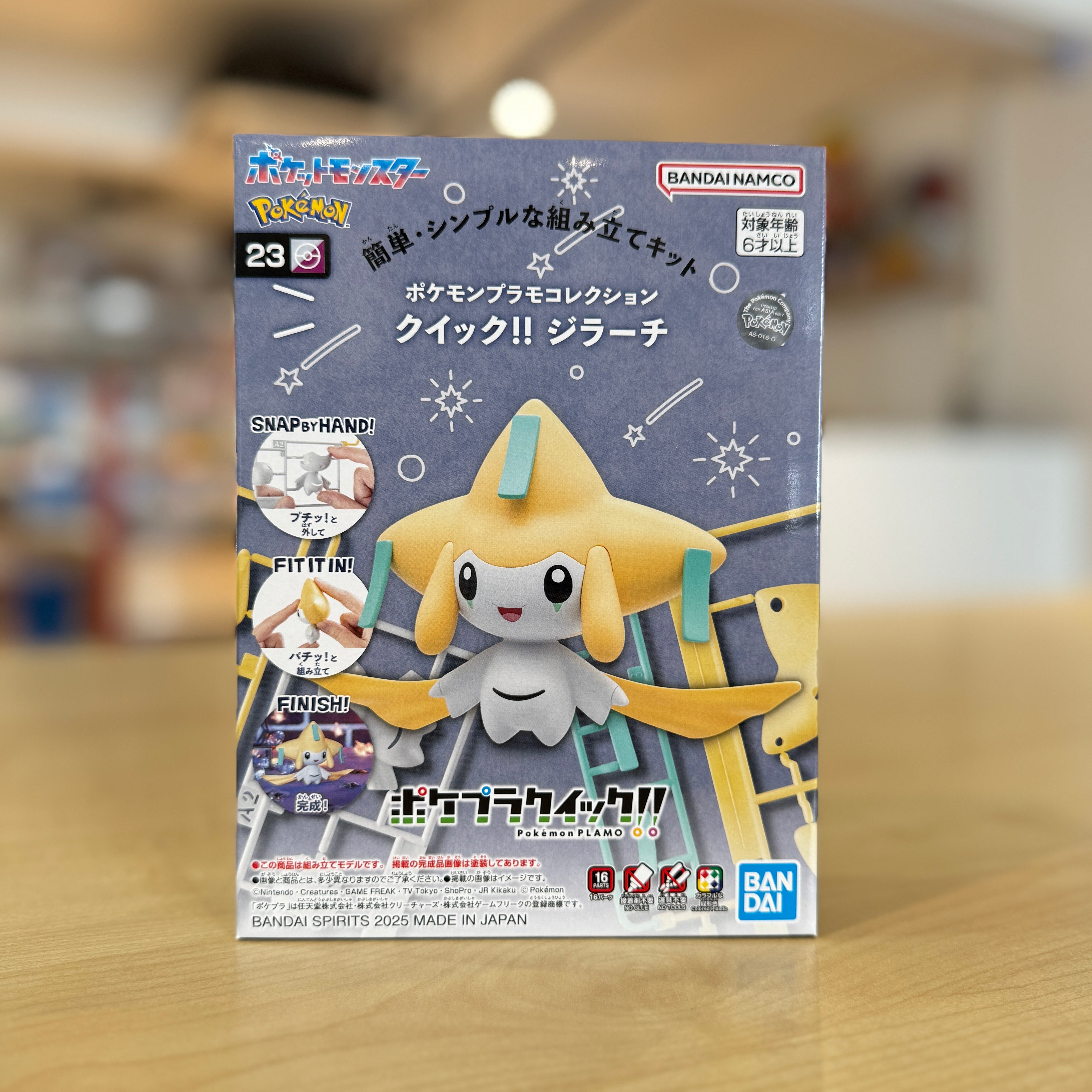 Pokémon Plamo Collection QUICK!! 23 – Jirachi figure packaging on a wooden surface.