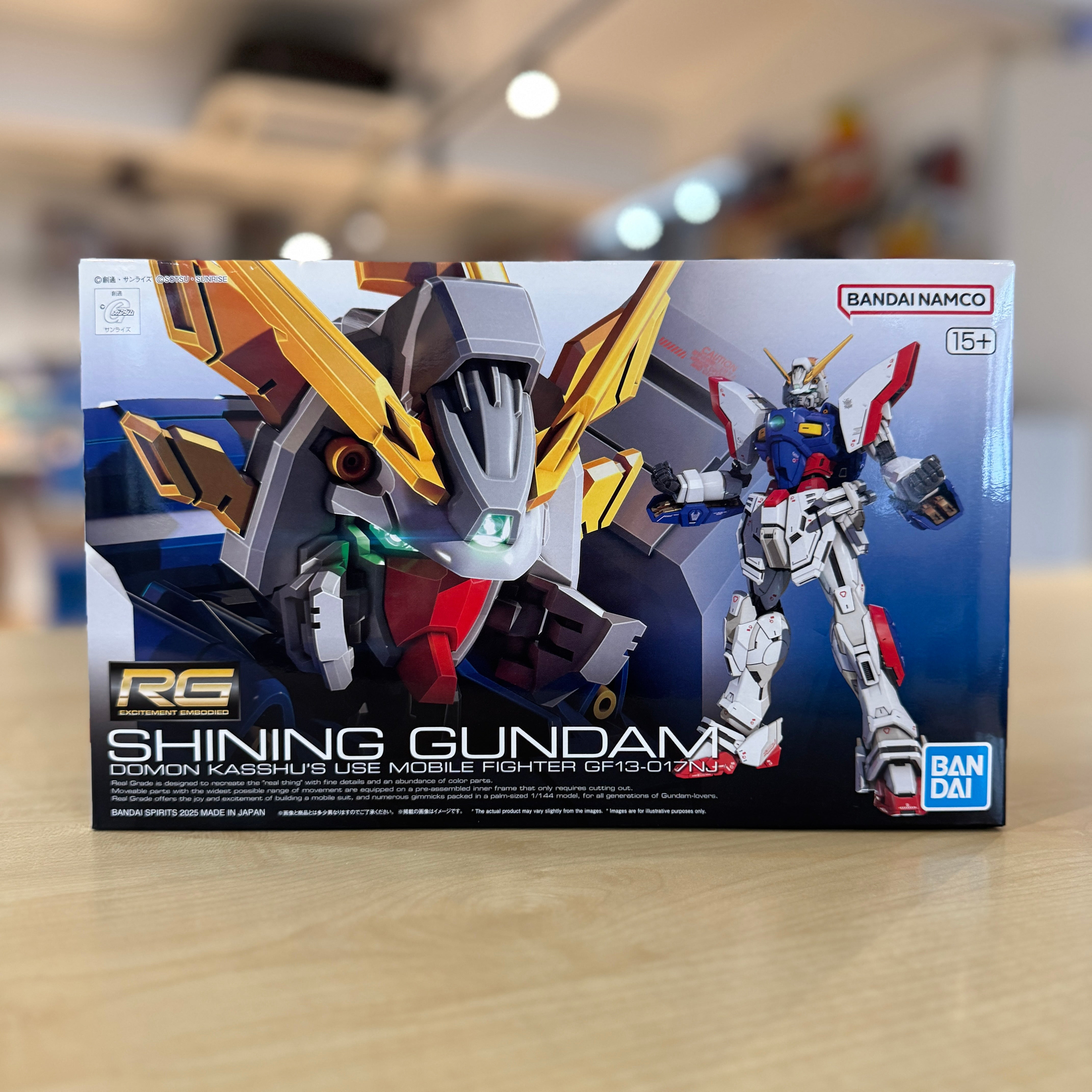 Box of RG Shining Gundam model kit by Bandai on a blurred indoor background